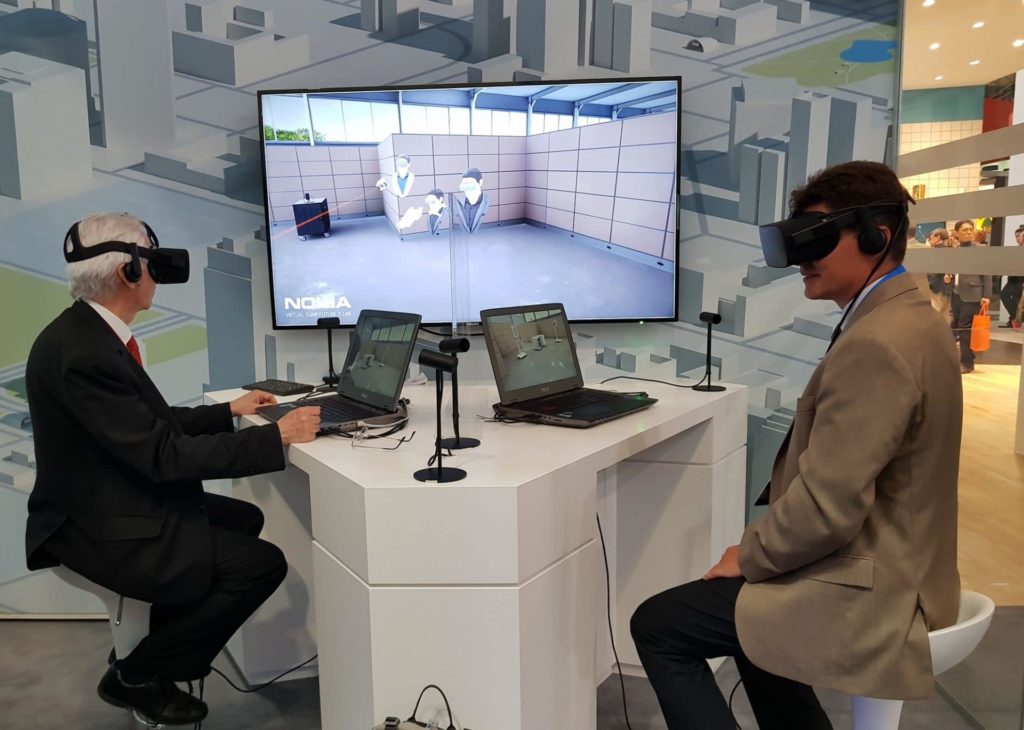 Kaksi henkilöä istumassa VR-lasit päässä ruudun lähellä.