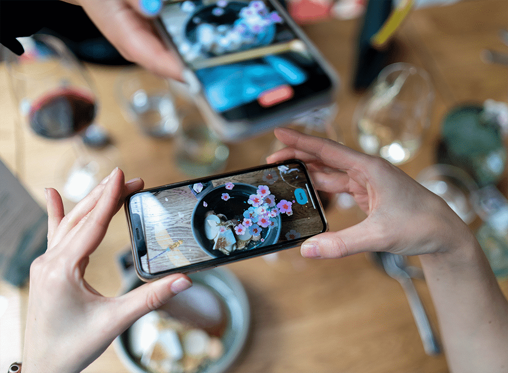Ruokapöydässä olevat lisätyn todellisuuden kukat, jotka näkyvät älypuhelimen ruudulta Ravintola Versionissa.